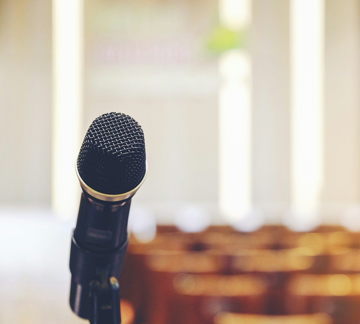 Nahaufnahme eines Mikrofons vor einem verschwommenen Hintergrund mit Stühlen.