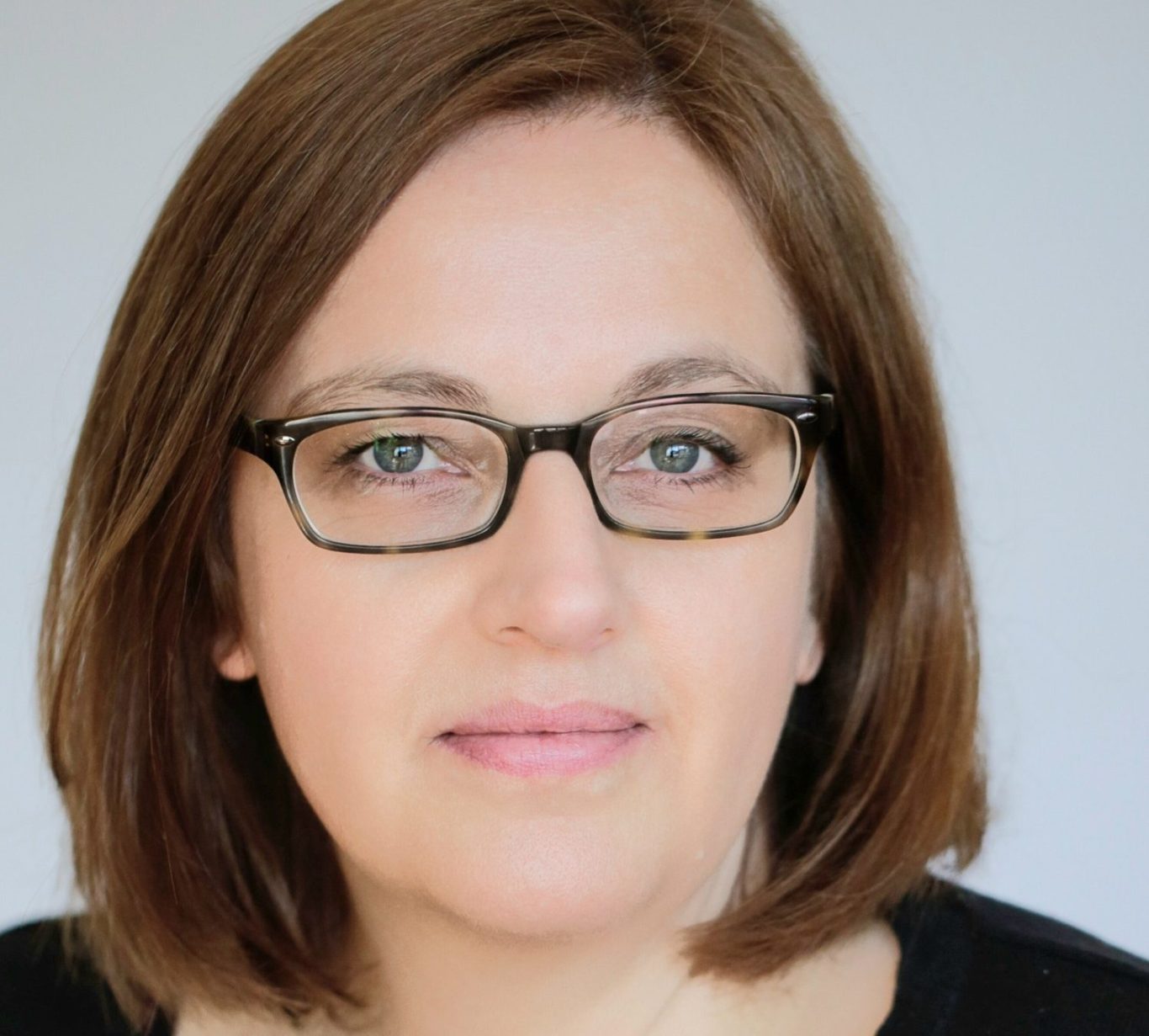 Porträt von Beate Kriechel mit Brille und schulterlangen braunen Haaren, neutraler Hintergrund.