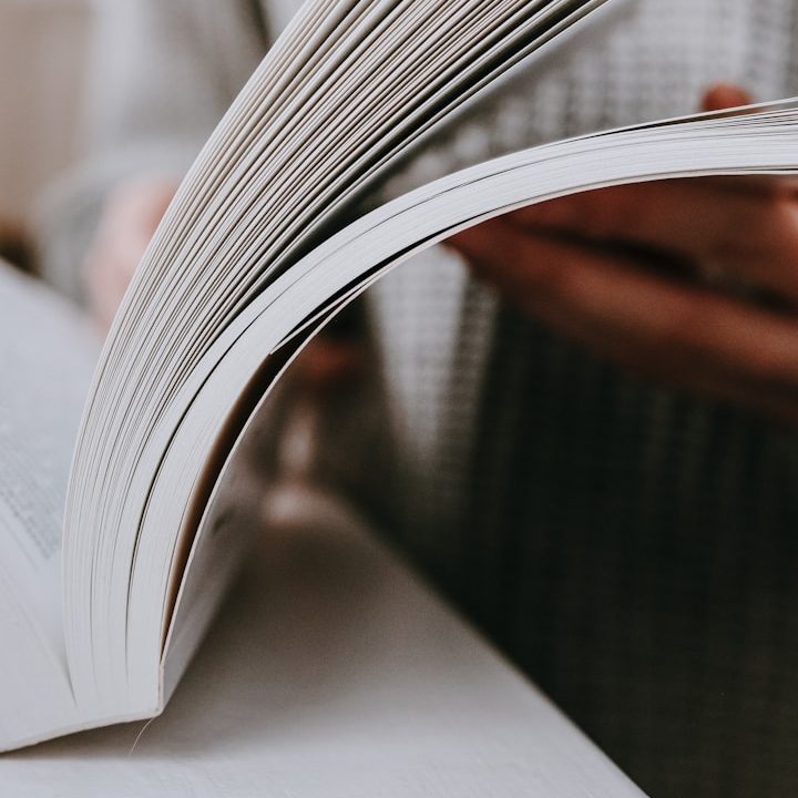 Eine Person blättert durch ein offenes Buch mit einem hellen Hintergrund.